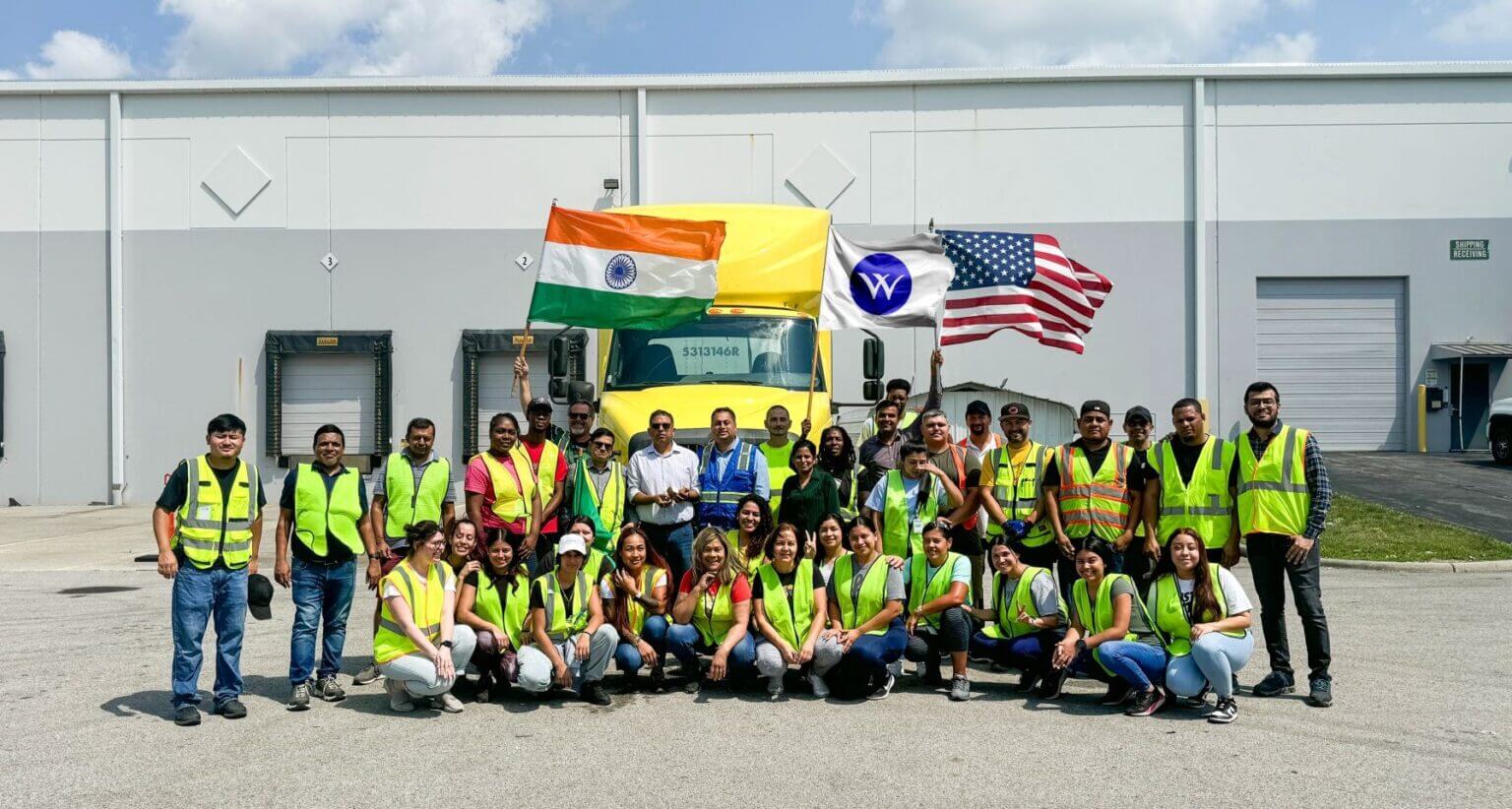 Warehouse team in safety vests posing with Indian, American, and Welspun flags.
