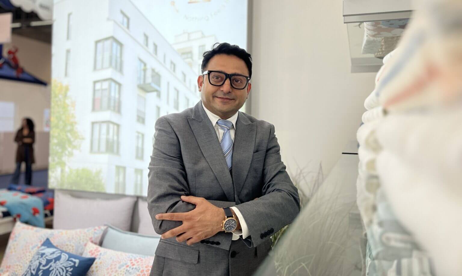 Man in a gray suit with glasses posing confidently in a modern showroom.