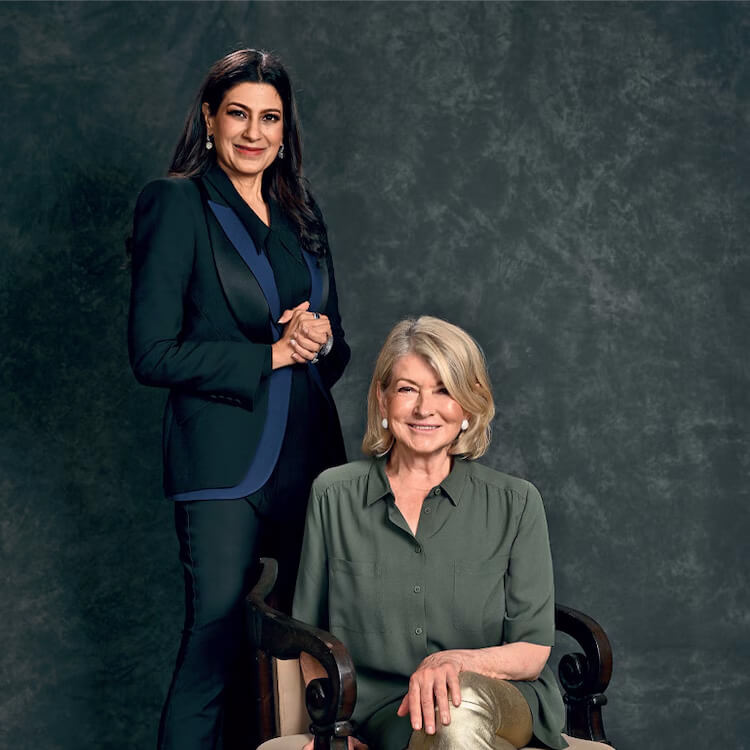 Two women posing together, one standing in a dark suit and the other seated in a green blouse.